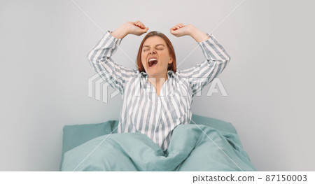 Beautiful young happy caucasian woman stretches after waking up in bed in the morning. Beautiful young happy caucasian woman stretches after waking up in bed in the morning. 87150003