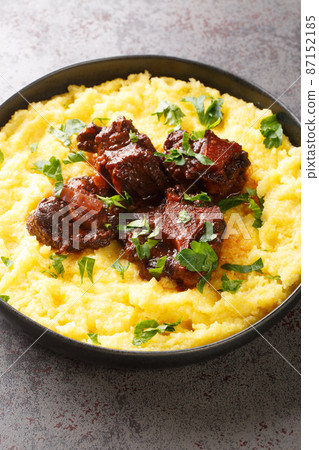 Brazilian traditional food stewed oxtail Rabada with corn polenta closeup on plate. Vertical 87152185