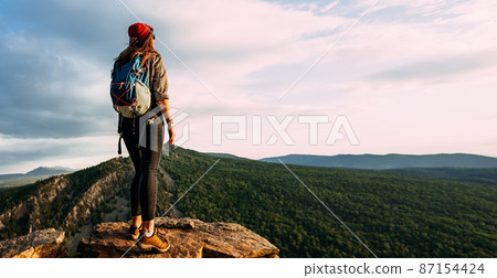 A lonely traveler with a backpack on the background of mountains, panorama. A female traveler in the mountains. A man in tourist gear on the background of mountains, rear view. Hiking in the mountains 87154424