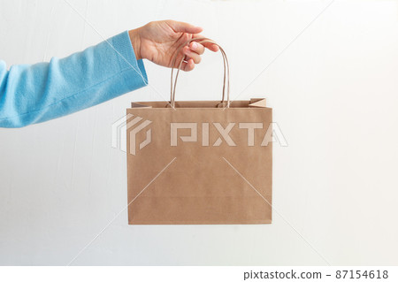 hand in a blue sweater holding a paper bag, against white background hand in a blue sweater holding a paper bag, against white background 87154618