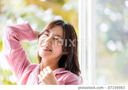 A refreshing woman standing by the window and bathing in the morning light A refreshing woman standing by the window and bathing in the morning light 87156983