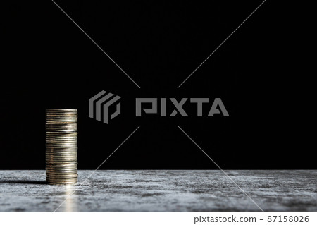 Stack of coins on grey table and black background with copy space 87158026