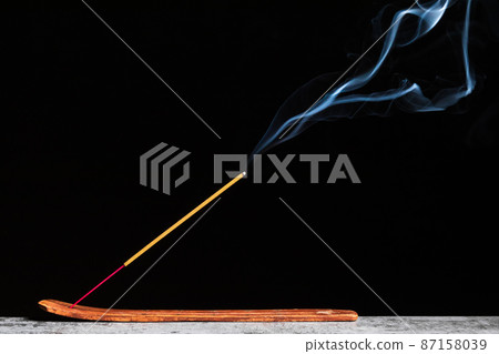 Burning stick of incense stands on a wooden stand isolated on a black background 87158039