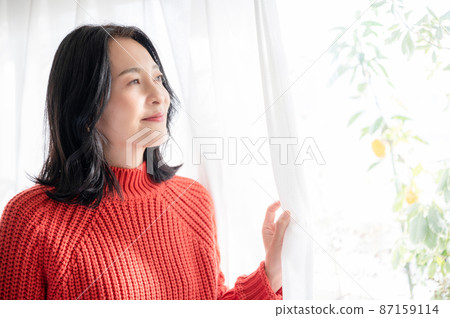 A beautiful Japanese (Asian) woman who opens the curtain in a bright backlit room and smiles at the sunrise. There is a copy space. 87159114