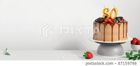 Banner with Chocolate birthday cake with berries, cookies and number eighty golden candles on White background, copy space 87159798