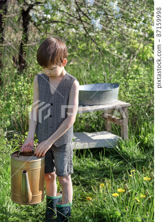 village boy in retro clothes with an iron watering can in the garden village boy in retro clothes with an iron watering can in the garden 87159998