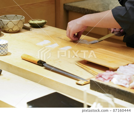 Chef use sharp knife slicing white  squid for sashimi. 87160444