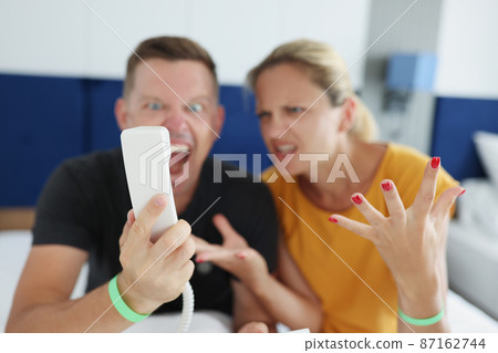 Couple yelling into phone while sitting on the bed in the hotel Couple yelling into phone while sitting on the bed in the hotel 87162744