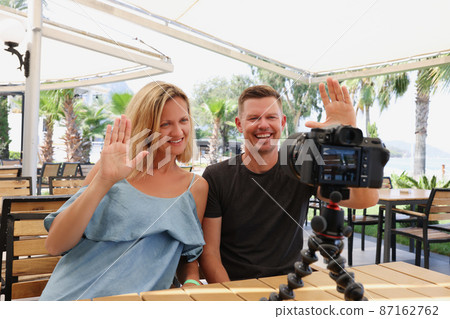 Happy couple waving at the camera on a tripod in a cafe 87162762