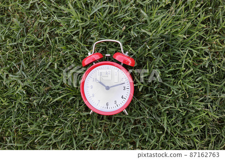 A red alarm clock on uncut green grass close-up 87162763