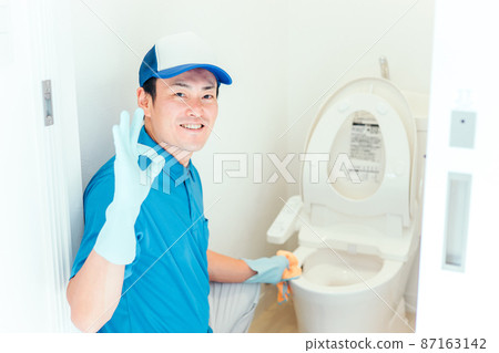A man in work clothes cleaning the toilet 87163142