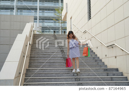 Beautiful girl is holding shopping bags, looking at camera and smiling while walking down the street Beautiful girl is holding shopping bags, looking at camera and smiling while walking down the street 87164965