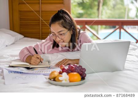 work from home, a young Asian woman who works in finance at home calculates financial graphs showing the results of his investments, planning the steps of his business growth work from home, a young Asian woman who works in finance at home calculates financial graphs showing the results of his investments, planning the steps of his business growth 87168489