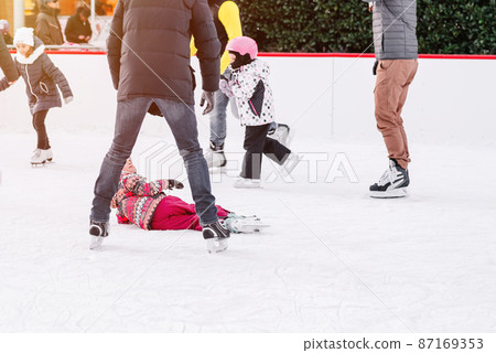 Soft,Selective focus.People, friendship, sport and leisure concept - happy friends on skating rink.Group of teenage friends ice skating on an ice rink.A kid takes relax after his fall while skating. 87169353