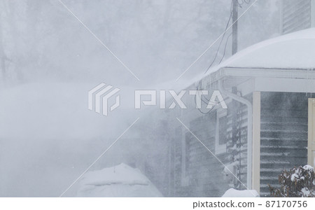 Snow blowing off a roof during a blizzard creating white out conditions 87170756