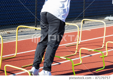 Athlete stariting to jump over plastic plastic mini hurdles on a track Athlete stariting to jump over plastic plastic mini hurdles on a track 87170757