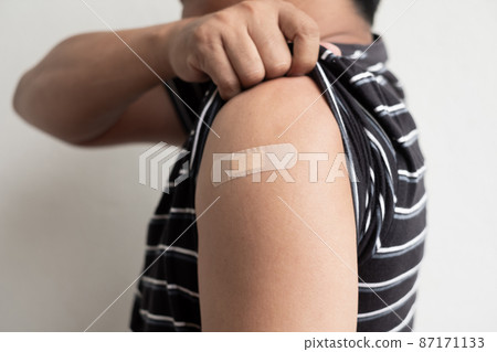 Asian man shows plaster on her shoulder after being vaccinated against Covid-19. Coronavirus vaccination campaign concept 87171133