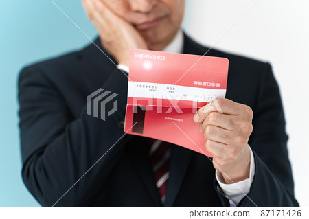 Senior businessman who is worried about looking at his passbook Senior businessman who is worried about looking at his passbook 87171426