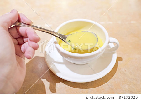 A spoon lifted with the left hand and corn soup in a cup A spoon lifted with the left hand and corn soup in a cup 87172029