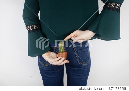Concept. A woman holds a cactus as a symbol of rectal pain. Varicose veins of the lower intestine. Pain in the rectum, hemorrhoids and pain in the excretory system of the body. Proctology 87172366