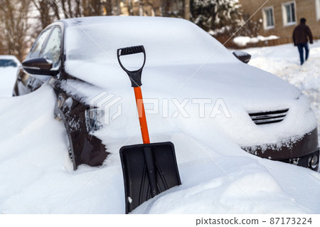 plastic snow shovel in front of snow-covered car at sunny winter morning 87173224