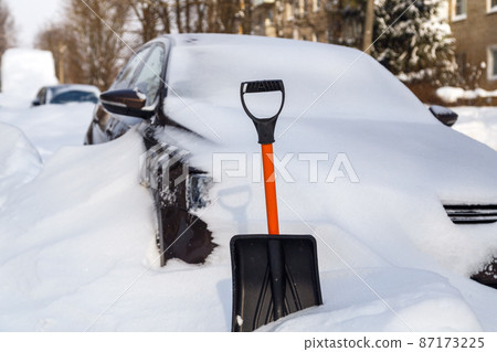 plastic snow shovel in front of snow-covered car at sunny winter morning plastic snow shovel in front of snow-covered car at sunny winter morning 87173225
