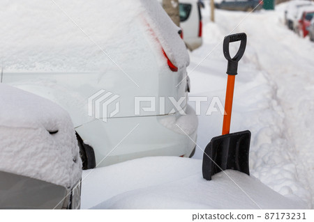 small plastic snow shovel near snow-covered cars at sunny winter morning small plastic snow shovel near snow-covered cars at sunny winter morning 87173231