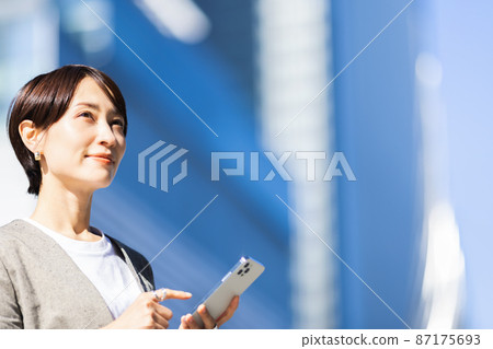 A woman operating a smartphone in the city 87175693