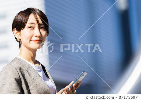 A woman operating a smartphone in the city 87175697