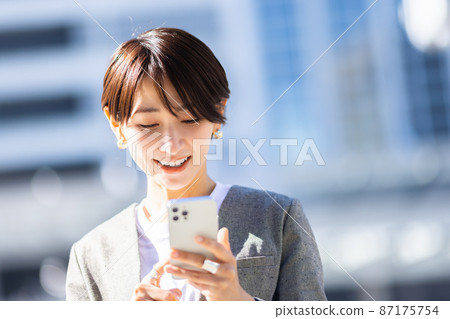 A woman operating a smartphone in the city 87175754