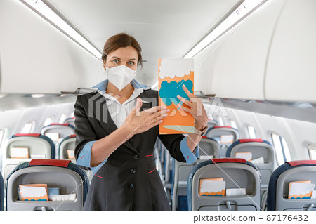 Woman stewardess in medical mask holding instruction booklet Woman stewardess in medical mask holding instruction booklet 87176432