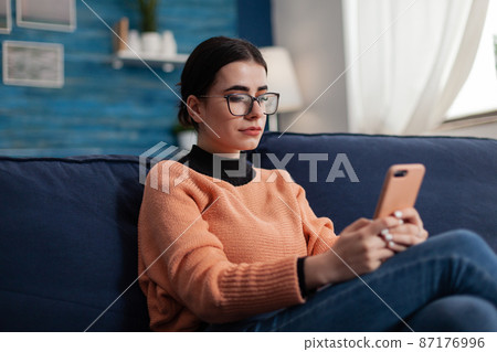 Student relaxing on couch holding smartphone and looking at screen. Student relaxing on couch holding smartphone and looking at screen. 87176996