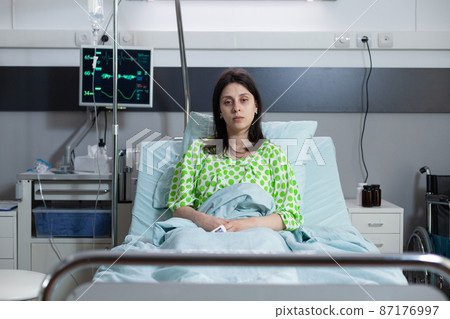 Patient sitting upright in hospital bed looking ill connected to monitor measuring vitals Patient sitting upright in hospital bed looking ill connected to monitor measuring vitals 87176997