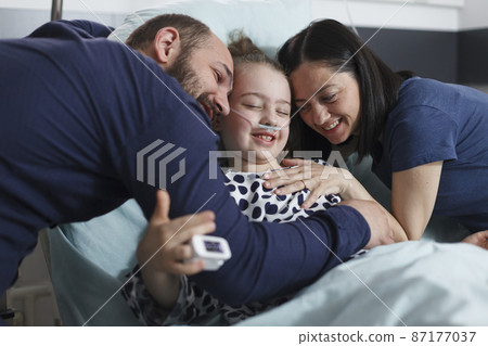 Happy young parents hugging hospitalized recovered little daughter while in pediatric clinic patient room. Happy young parents hugging hospitalized recovered little daughter while in pediatric clinic patient room. 87177037