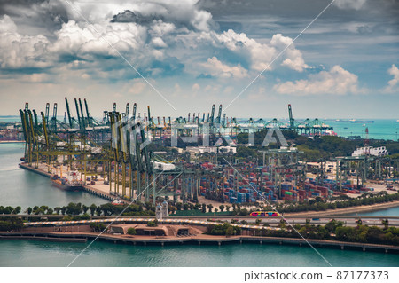 The huge busiest logistic port in Singapore, plenty of cranes to move containers, huge cargo ships in the background, skyscrapers on background The huge busiest logistic port in Singapore, plenty of cranes to move containers, huge cargo ships in the background, skyscrapers on background 87177373