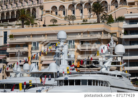 A lot of huge yachts are in port of Monaco at sunny day, Monte Carlo, real estate housing is on background, glossy board of the motor boat, megayachts are moored in marin 87177419