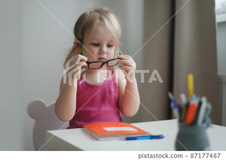 small funny girl in eyeglasses sitting at the table small funny girl in eyeglasses sitting at the table 87177487