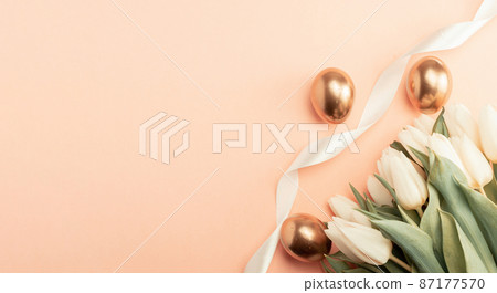 Golden eggs with spring white tulips on pastel pink background in Happy Easter decoration. Foil minimalist egg design, modern top view banner design. Golden eggs with spring white tulips on pastel pink background in Happy Easter decoration. Foil minimalist egg design, modern top view banner design. 87177570