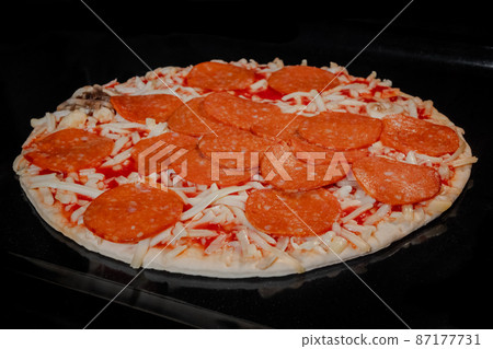 Uncooked homemade pizza on tray in electric oven, black background Uncooked homemade pizza on tray in electric oven, black background 87177731