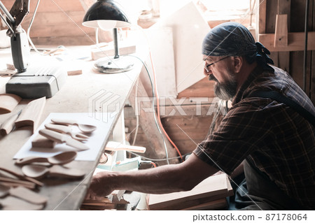 Spoon master in his workshop with wooden products and tools selecting right wood to make wooden kitchenware products. 87178064