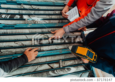 Geological gold core samples with team of mining workers measuring drilled rock top view. Selective focus Geological gold core samples with team of mining workers measuring drilled rock top view. Selective focus 87178147