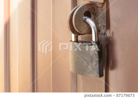 Close-up padlock on the gate of a metal brown fence made of modern siding, the concept of security Close-up padlock on the gate of a metal brown fence made of modern siding, the concept of security 87179873