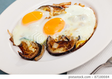Fried sunny side up eggs with eggplant and onions 87180084