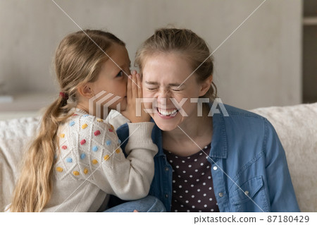 Cute kid telling secret to happy laughing elder sister, nanny 87180429
