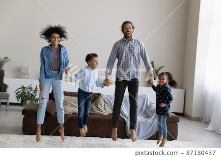 Happy active African American family jumping in modern living room. Happy active African American family jumping in modern living room. 87180437