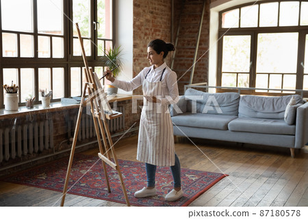 Full length creative millennial Indian woman drawing on easel. 87180578