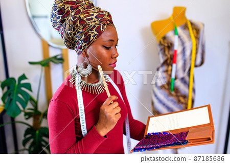 latin hispanic woman with fashionable turban over head and red dress working in clothess making office 87185686