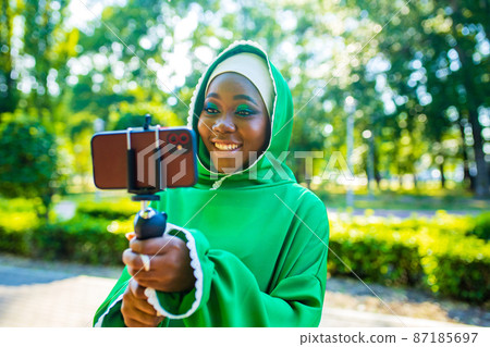 latin hispanic wonan in green muslim hijab with bright make up and nose piercing taking video stream outdoors summer park latin hispanic wonan in green muslim hijab with bright make up and nose piercing taking video stream outdoors summer park 87185697