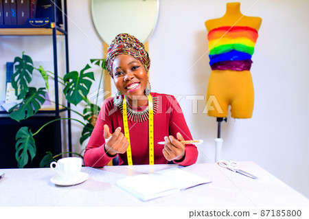 tanzanian woman with snake print turban over hear creating a colorful dress for pride parade in her dressmaking showroom 87185800