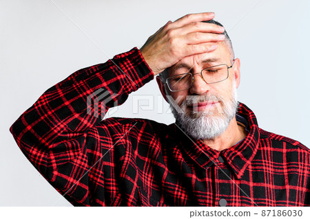 Portrait of mature man isolated on grey background suffering from severe headache, closing eyes to relieve pain 87186030